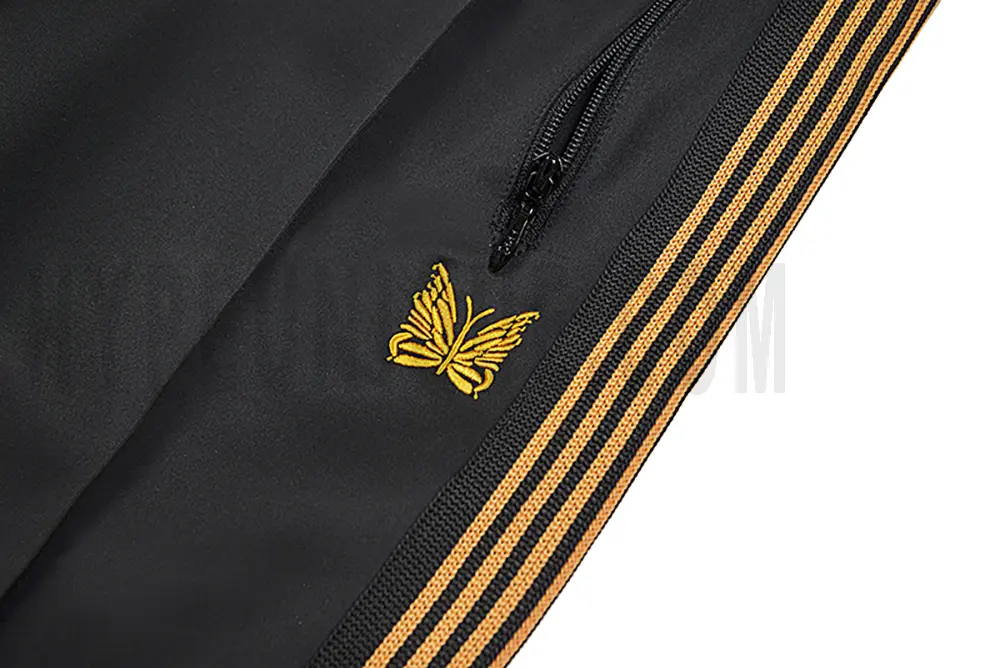 Close-up detail of the track pants pocket and delicate butterfly embroidery.