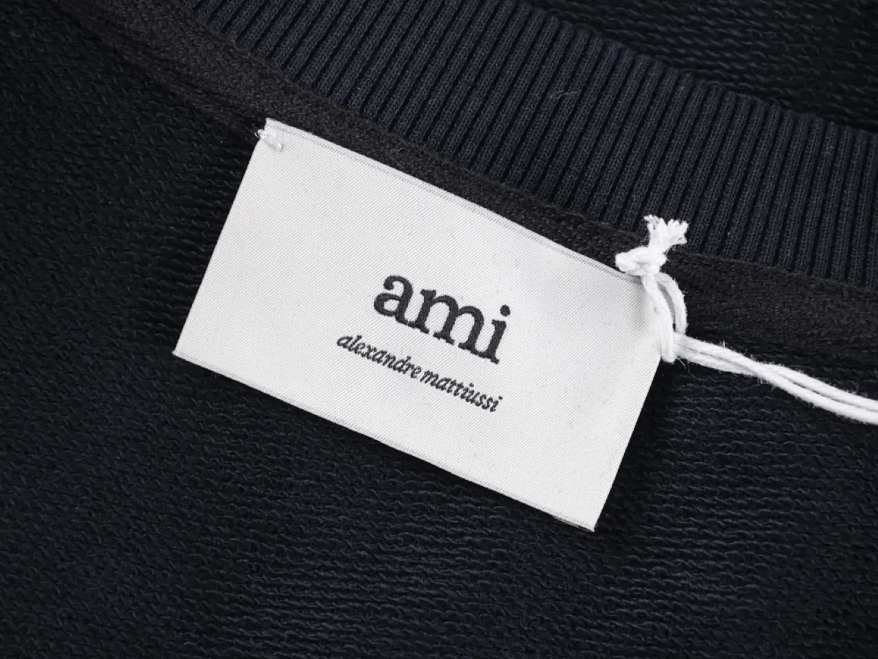 Label attached to a black cotton sweater with ribbed collar.