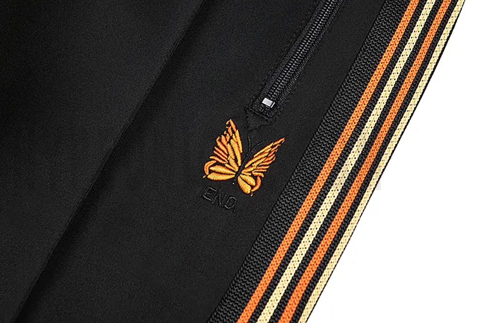 Close-up detail of the track pants pocket and delicate butterfly embroidery.