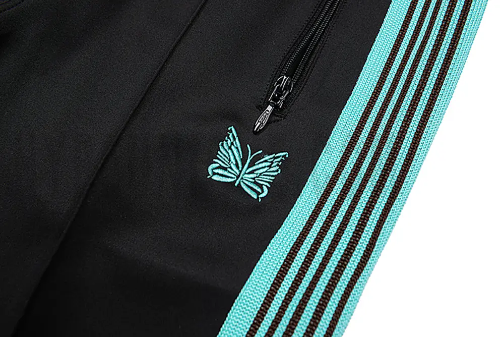 Close-up detail of the track pants pocket and delicate butterfly embroidery.