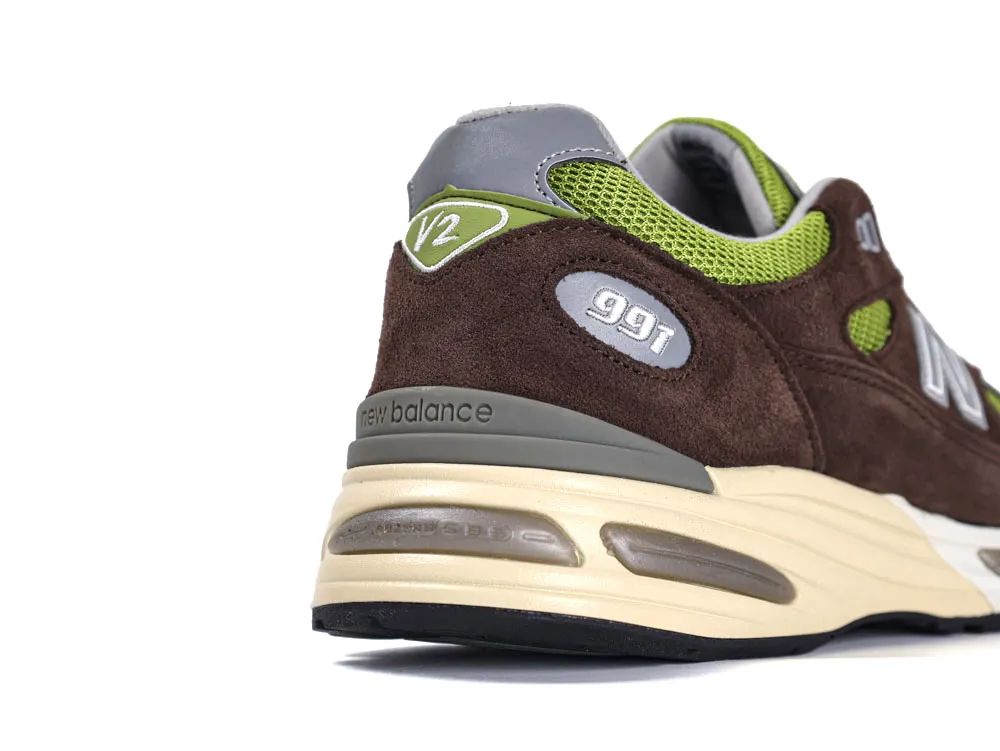 Brown suede sneaker with green mesh and beige rubber sole, New Balance logo visible.