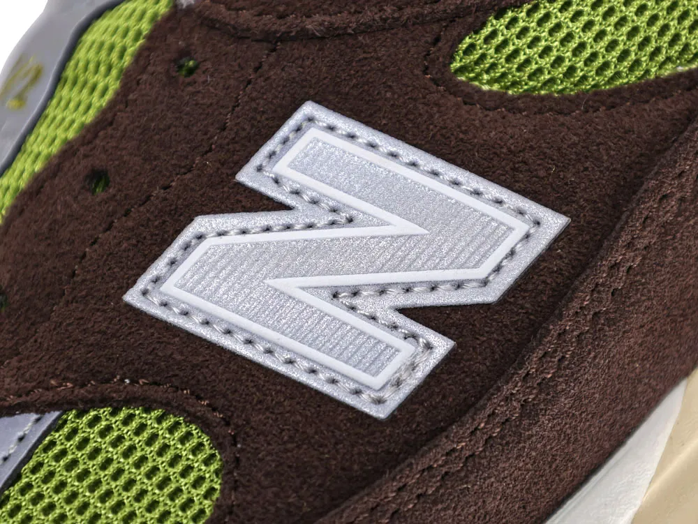 Brown suede sneaker with green mesh and white stitched emblem detail.