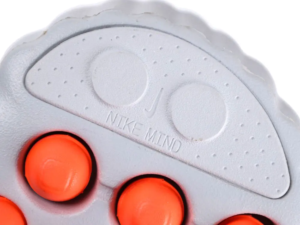 White rubber shoe sole with embossed text design and bright orange circular elements.