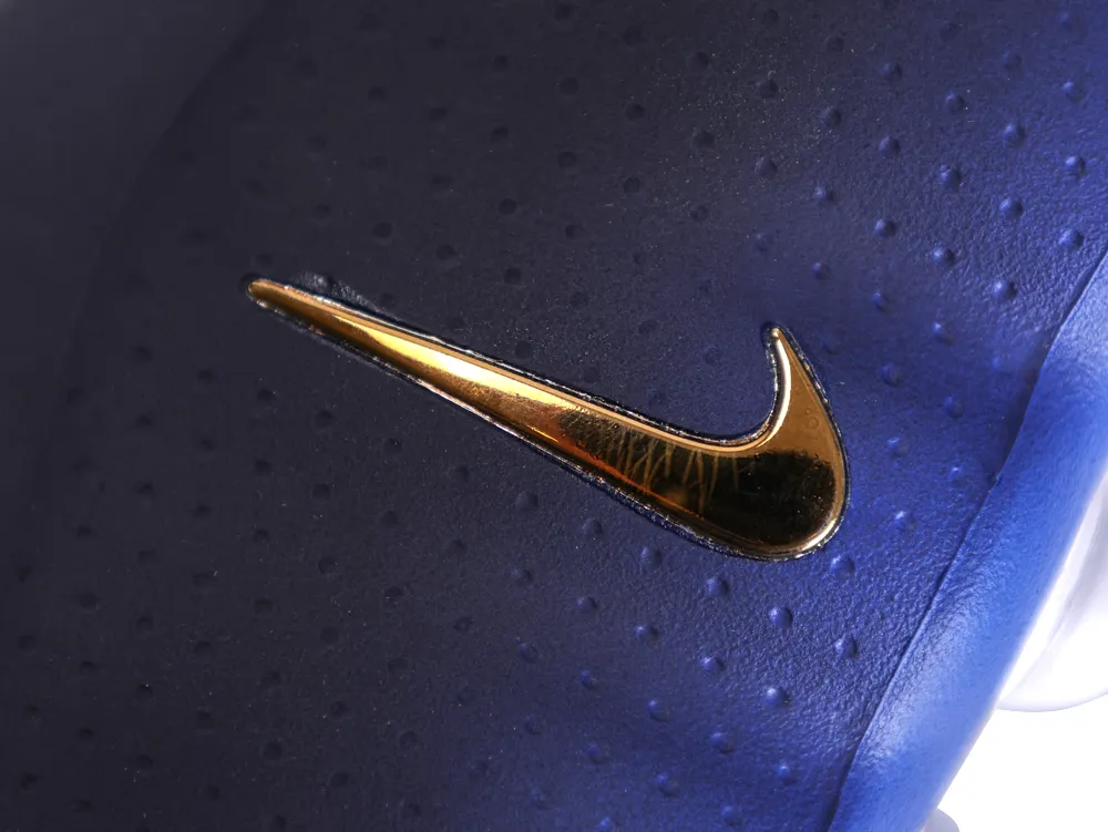 Close-up of a metallic gold Nike swoosh on the textured navy blue side panel.