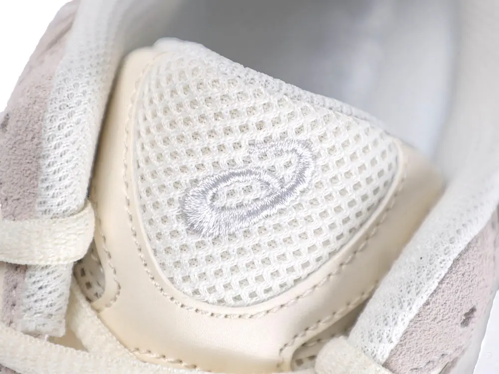 Close-up of a beige mesh sneaker tongue with suede and fabric details.