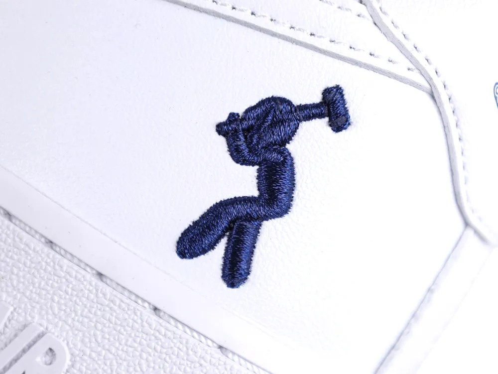 White leather sneaker with blue embroidered design on the side panel.