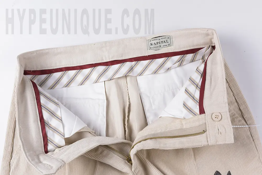 Interior waistband view of the KAPITAL Ivy Wide-Leg Pleated Printed Cotton-Corduroy Trousers, featuring a cotton lining and red binding tape.