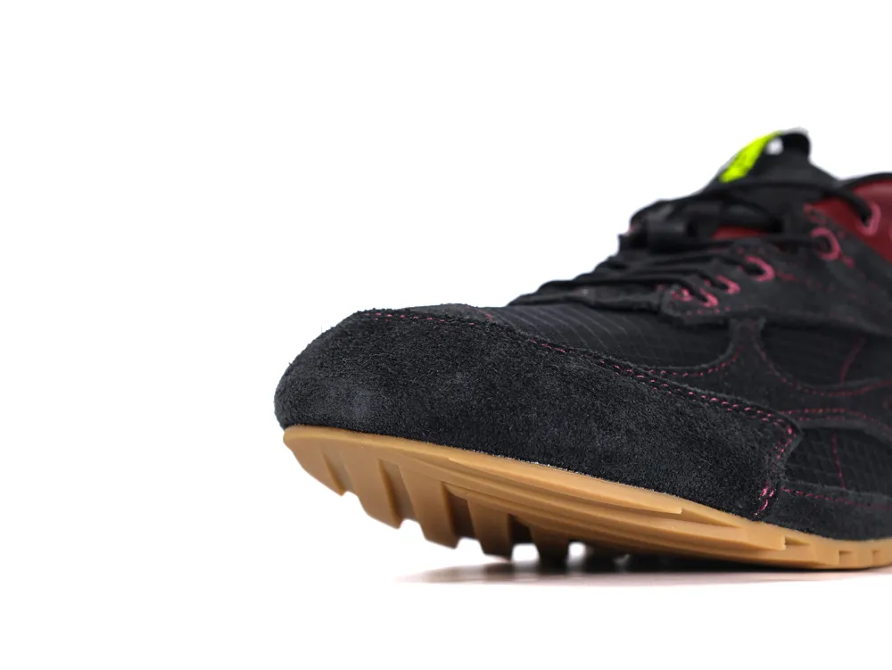 Close-up of black suede sneaker with gum sole and red stitching details.