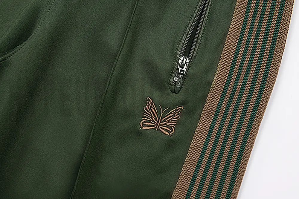 Close-up detail of the track pants pocket and delicate butterfly embroidery.