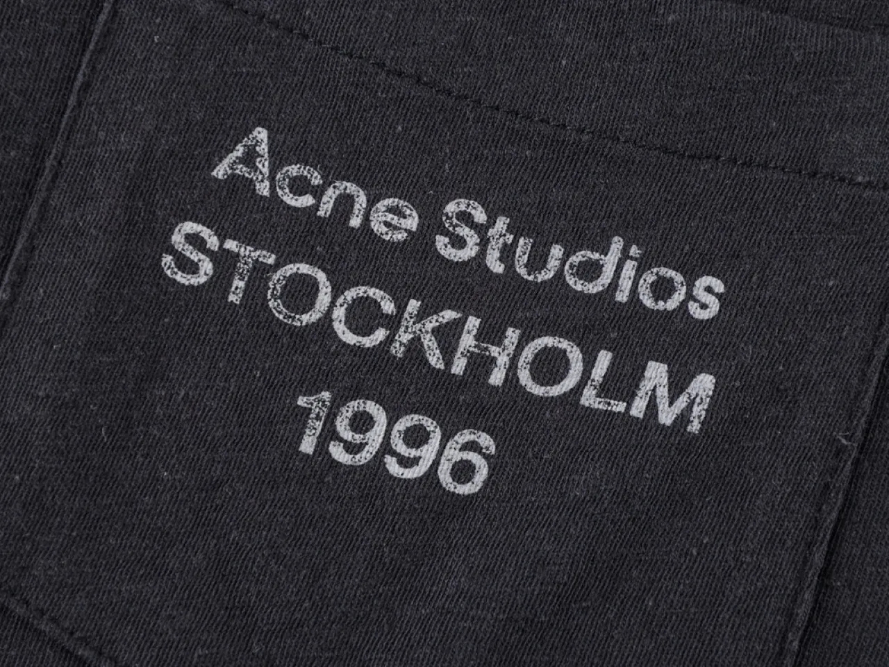 Close-up of black fabric with white printed text, featuring pocket detail.
