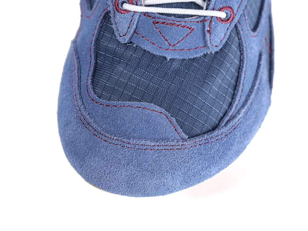 Close-up of blue suede and fabric sneaker toe, featuring red stitching detail.