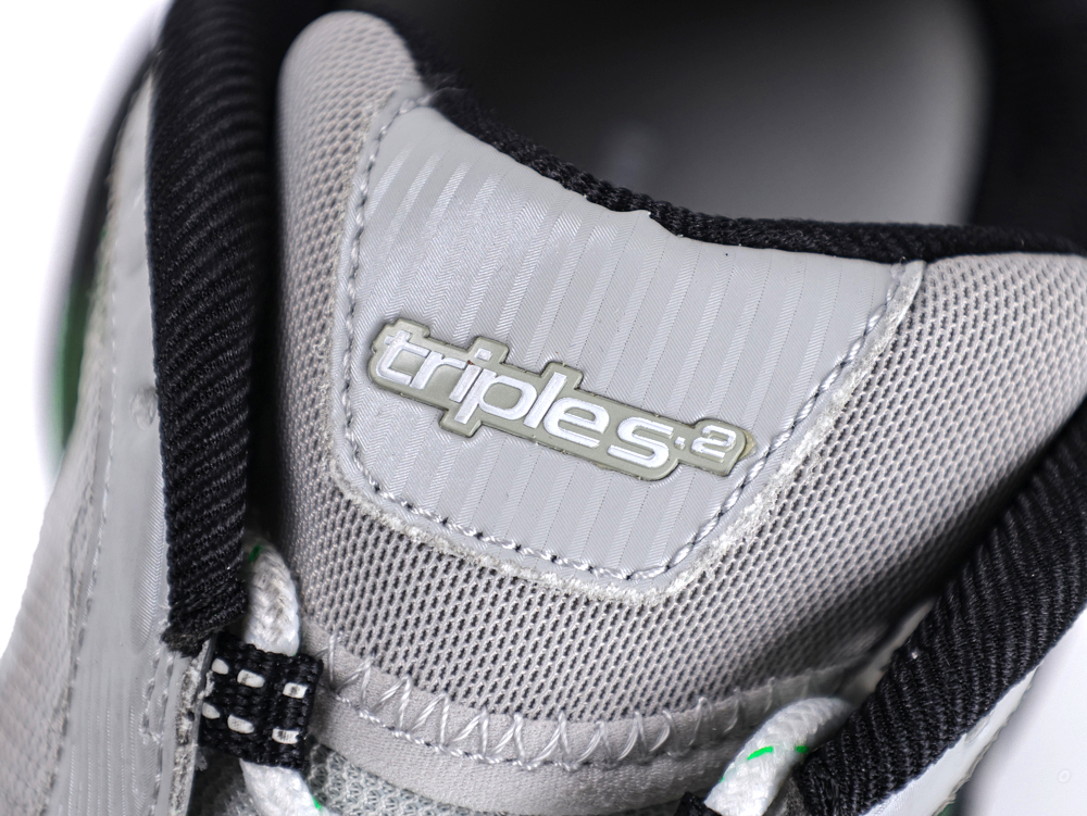 Close-up of a gray sneaker tongue with "triples" text, featuring black accents.