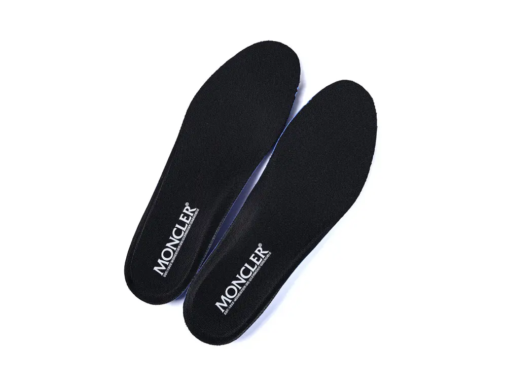 Two black shoe insoles with "MONCLER" branding in white text are placed diagonally against a white background.