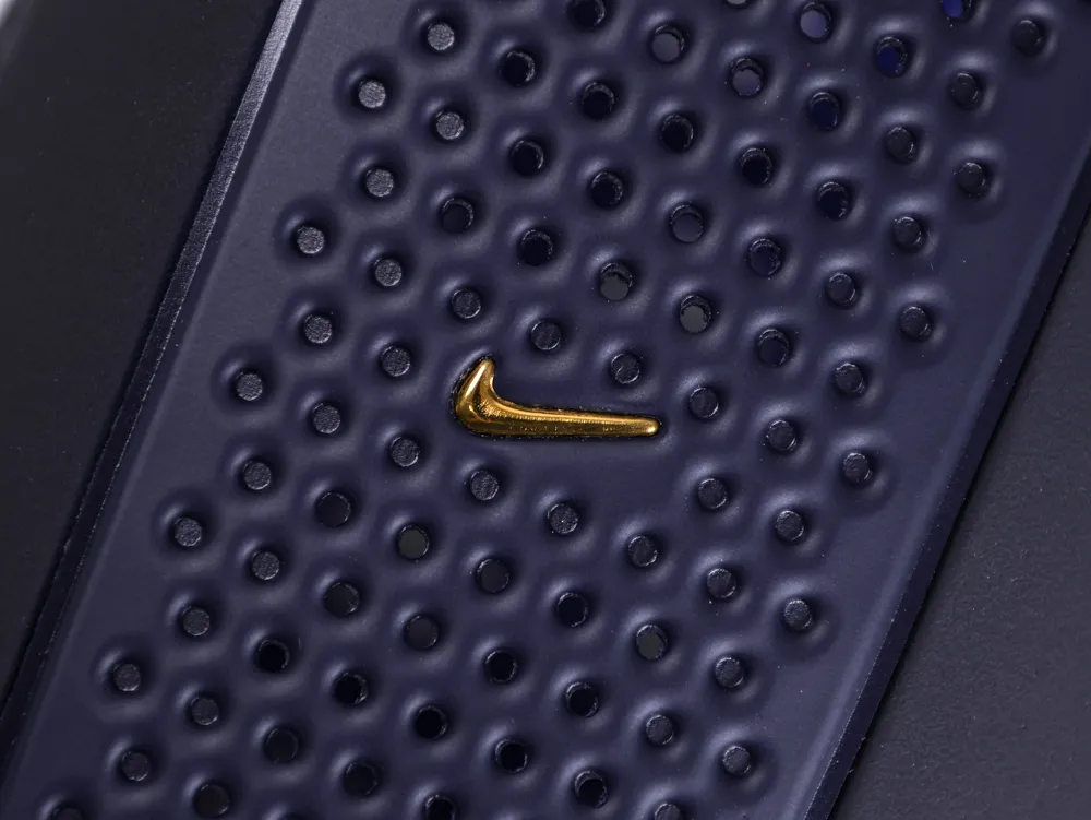 Detailed view of a tiny gold Nike swoosh centered on a perforated navy blue section of the shoe.