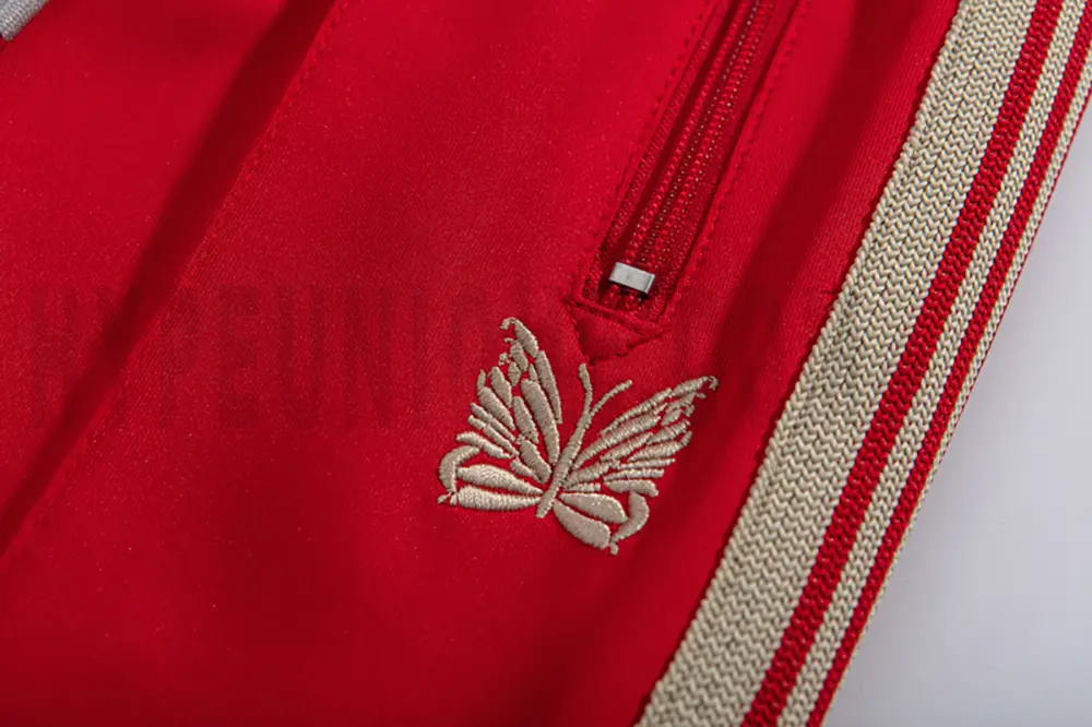 Close-up detail of the track pants pocket and delicate butterfly embroidery.