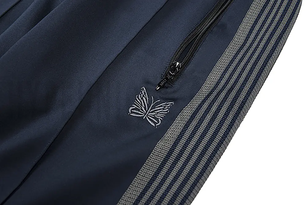 Close-up detail of the track pants pocket and delicate butterfly embroidery.