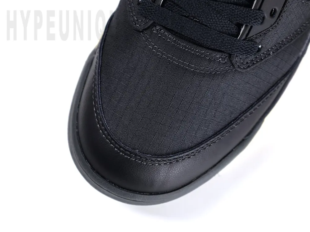Top-down view of the toe area on the Jordan 5 Retro PSG Paris Saint-Germain ‘Off Noir’, featuring a black leather mudguard and black woven fabric toe box.