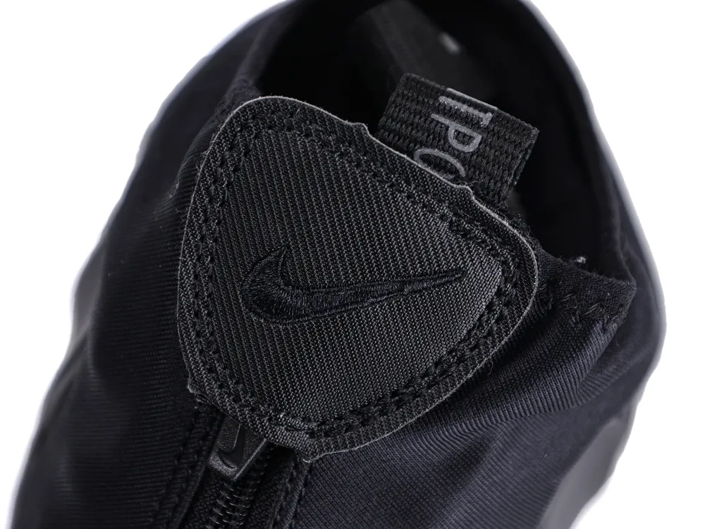 Close-up of a black fabric shoe with a zipper and stitched logo.