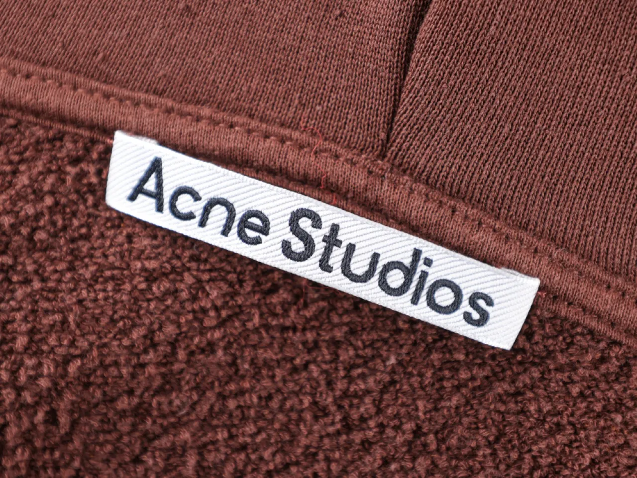 Brown wool texture with ribbed fabric and white "Acne Studios" label tag.