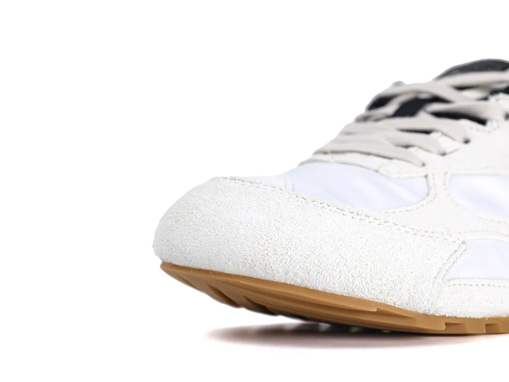 White suede sneaker toe with brown rubber sole, highlighting shoe's texture and color contrast.