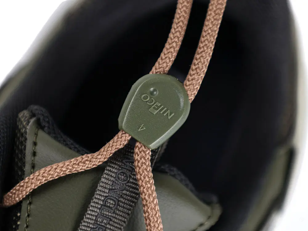Close-up of a shoe's olive green toggle and brown laces, contrasting with black and dark green fabric materials.