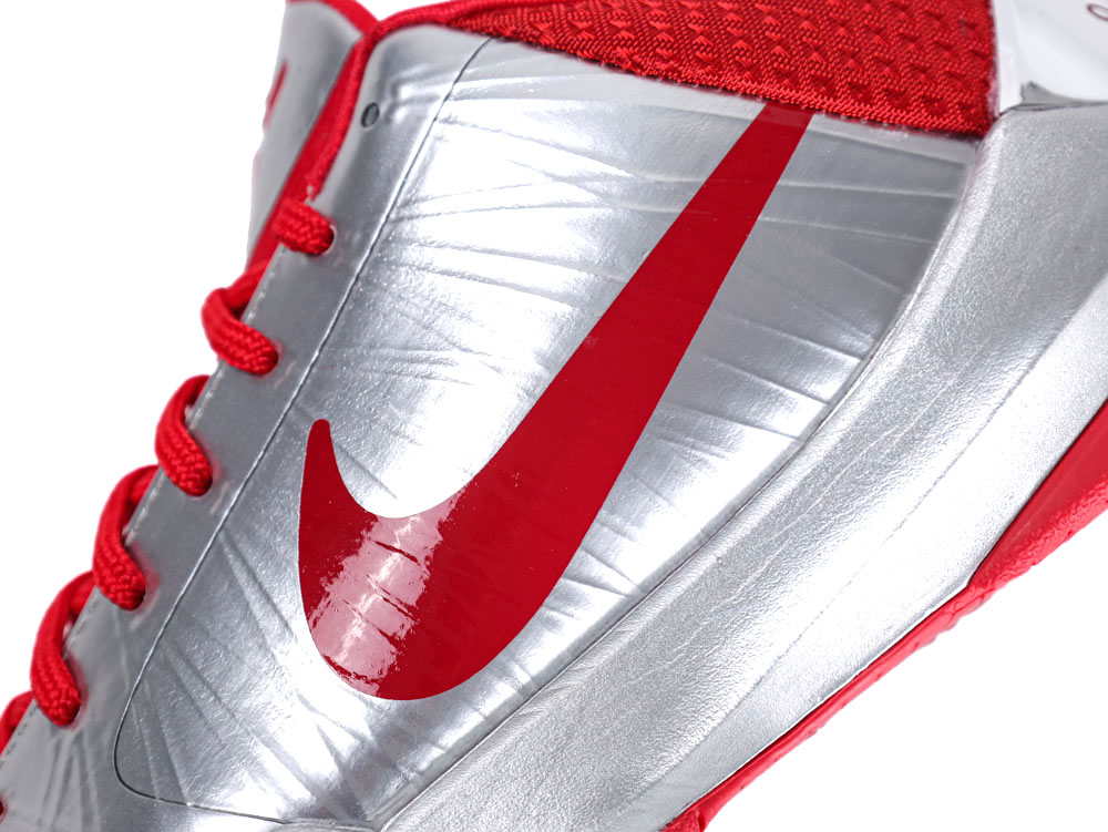Close-up of a silver shoe with a red logo and red laces.