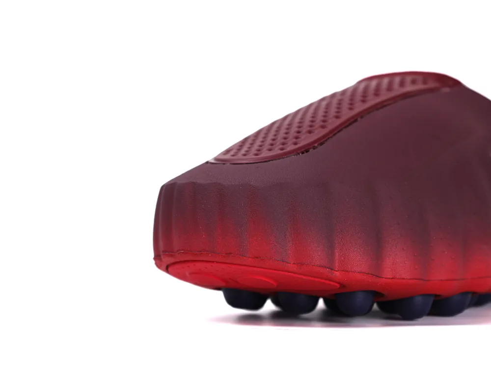 A low-angle front view of the burgundy textured upper and black traction pods on the red sole.