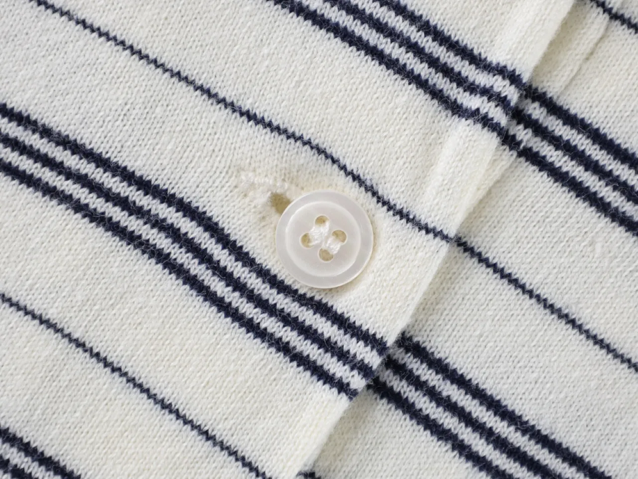Close-up of a white knit fabric with navy stripes and a button.