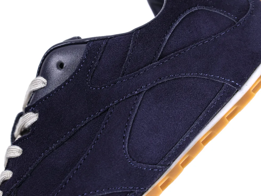 Close-up of a navy suede sneaker with white laces and a tan sole.