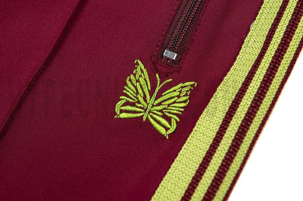 Close-up detail of the track pants pocket and delicate butterfly embroidery.
