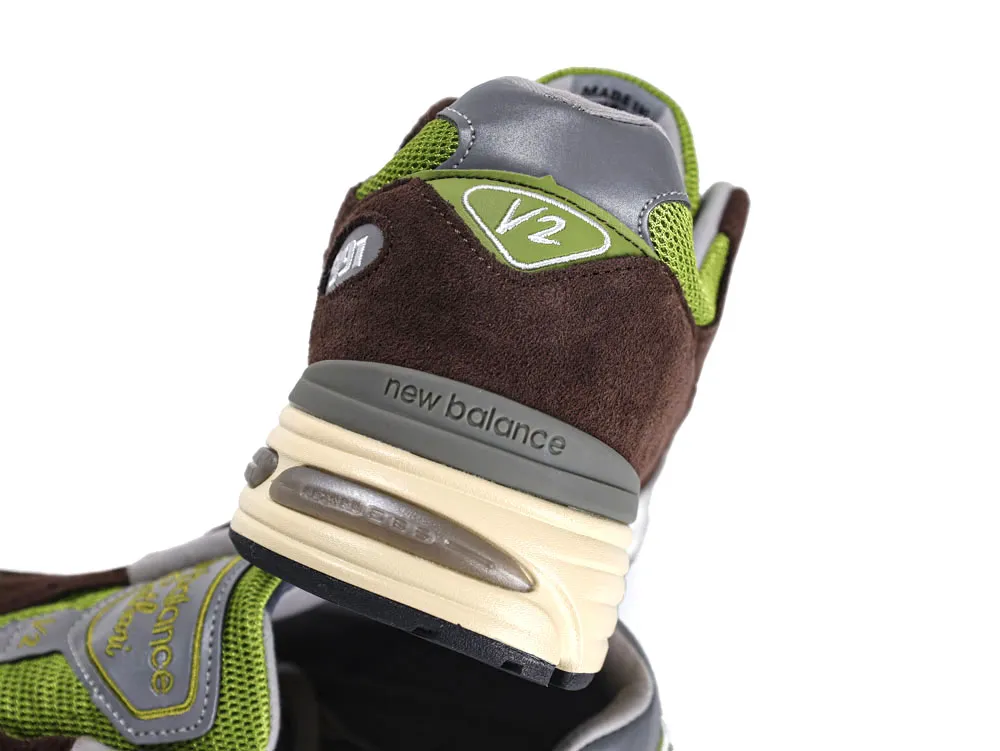Brown suede sneaker with green mesh accents and cream sole, featuring logo details.