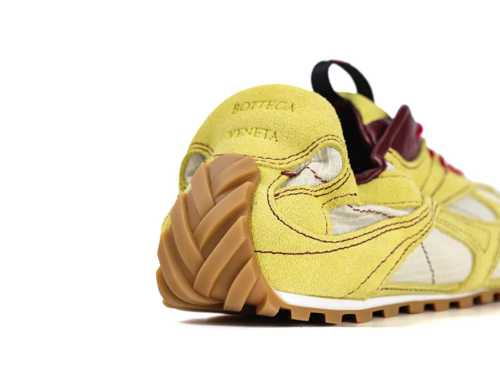 Yellow suede sneaker with gum sole and detailed stitching, showing the heel.