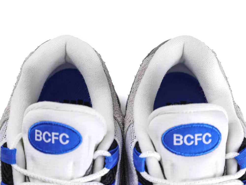 Gray and white sneakers with blue detailing and embroidered logo on tongue.