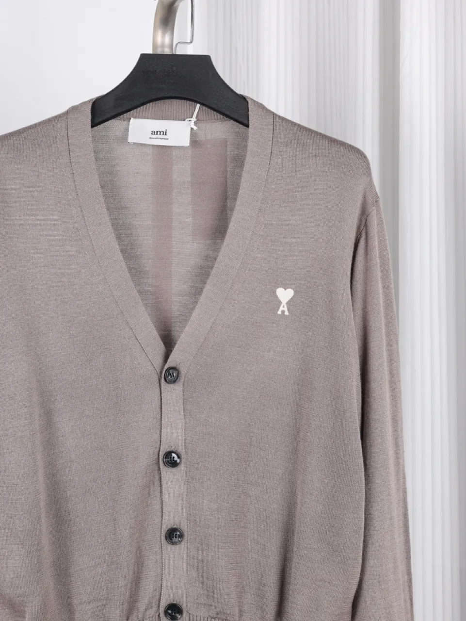 Taupe cardigan made of knit fabric with black buttons and a heart logo.