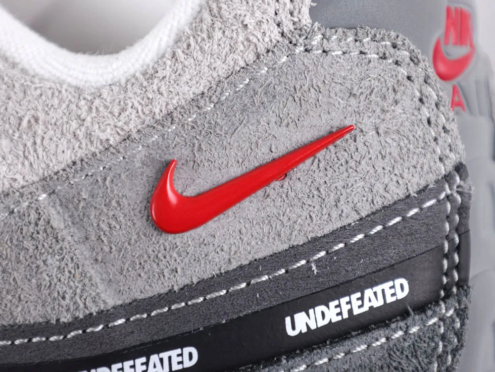 Gray suede shoe with a red logo and "Undefeated" text on the sole.