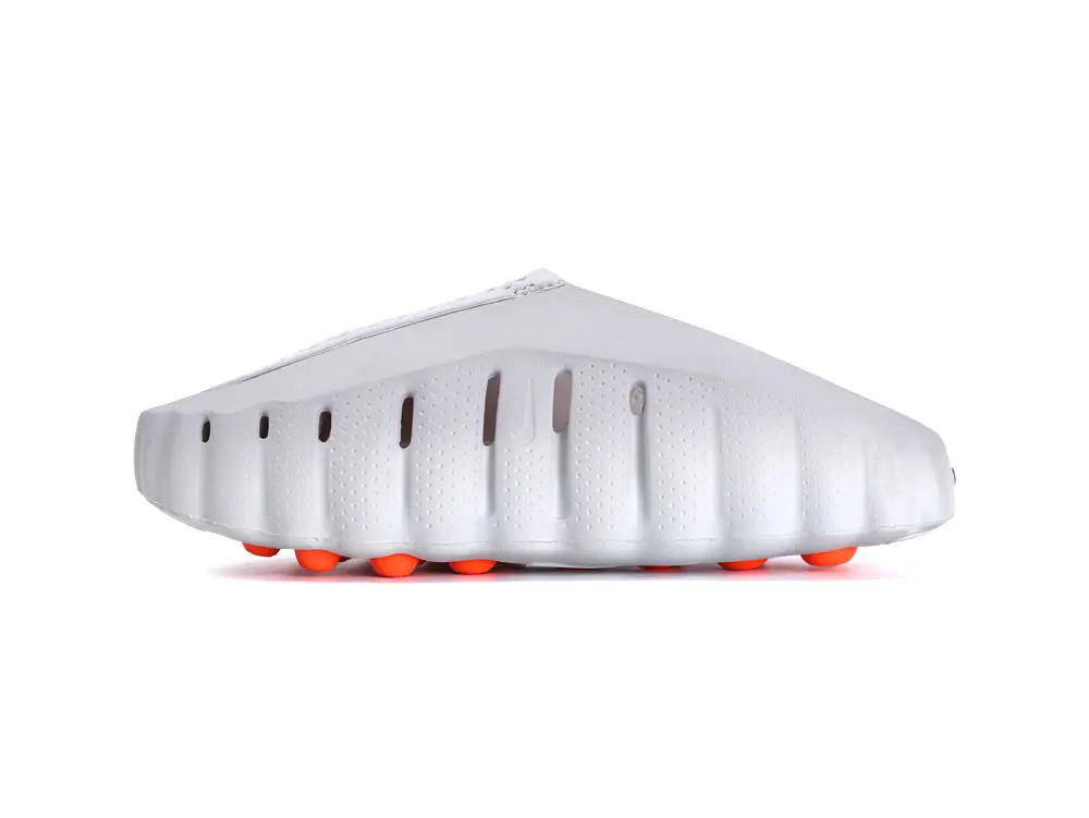 White synthetic sneaker with textured sole and orange circular grips underneath.