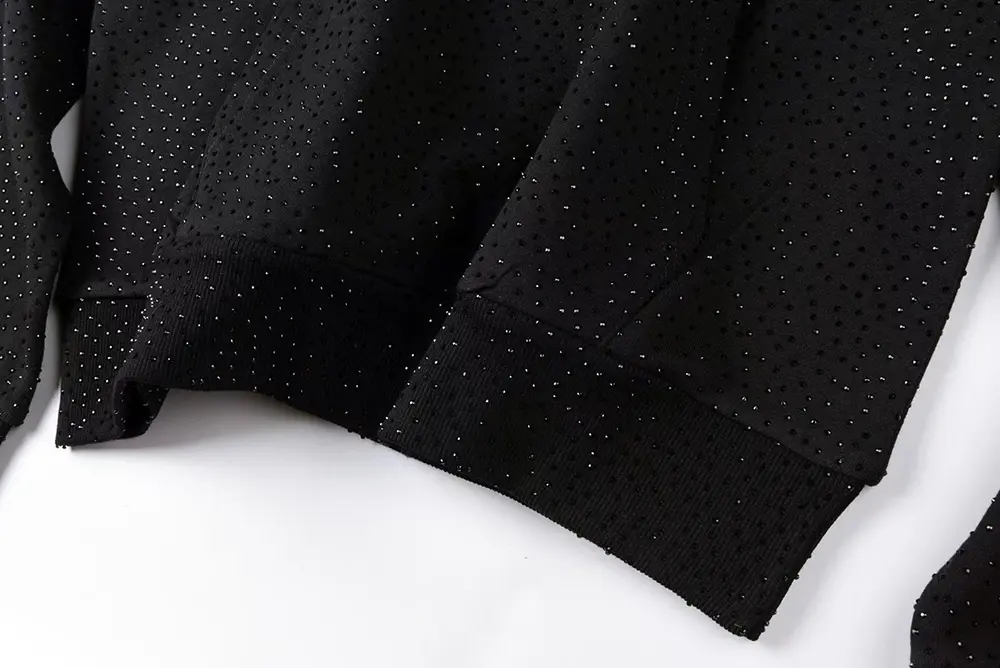 A top-down view of the sleeve of the Sp5der VVS Hoodie in Black, highlighting its cotton and polyester material and full rhinestone detailin