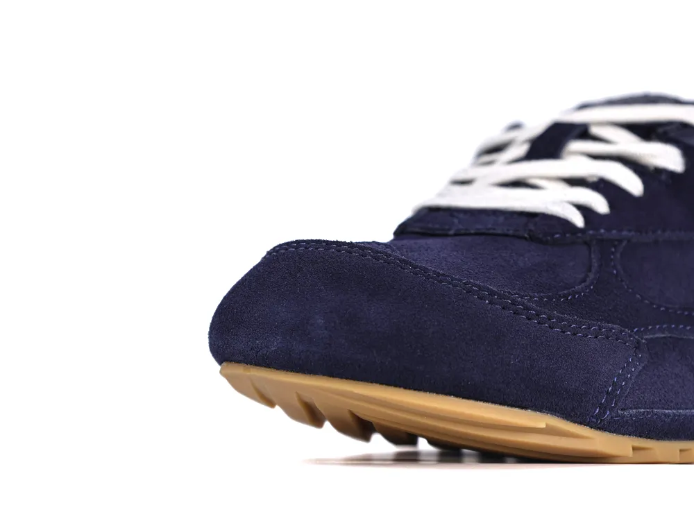 Navy suede shoe close-up featuring white laces and tan rubber sole.
