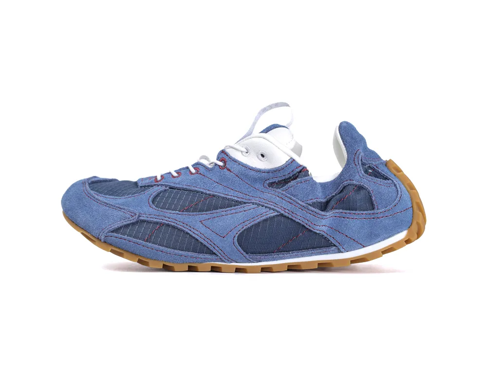 Blue denim sneaker with stitched panels, white eyelets, and a brown rubber sole.